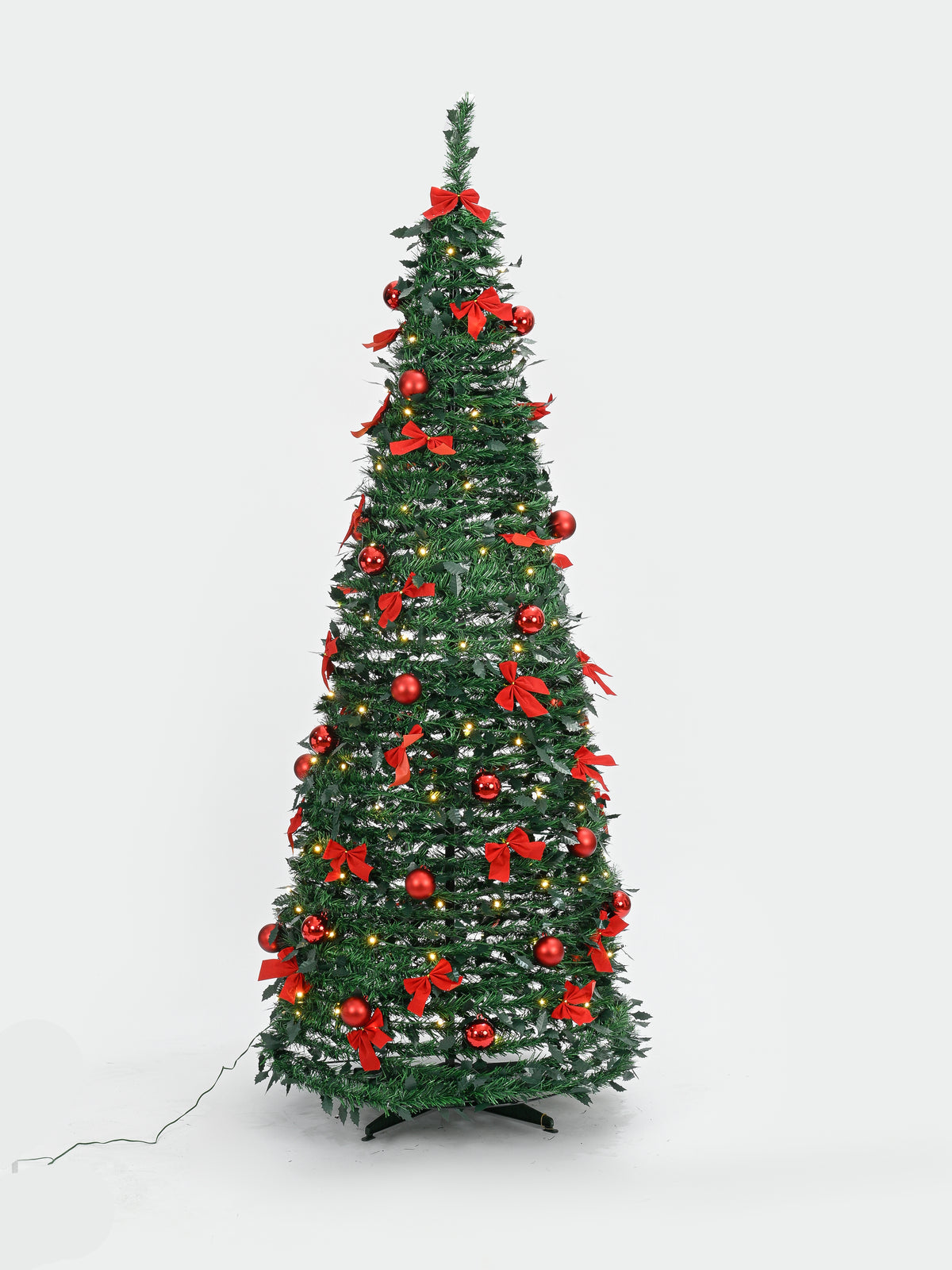 A decorated artificial Christmas tree with green branches, red bows, red ornaments, and small warm white lights, shown on a plain light gray studio background.